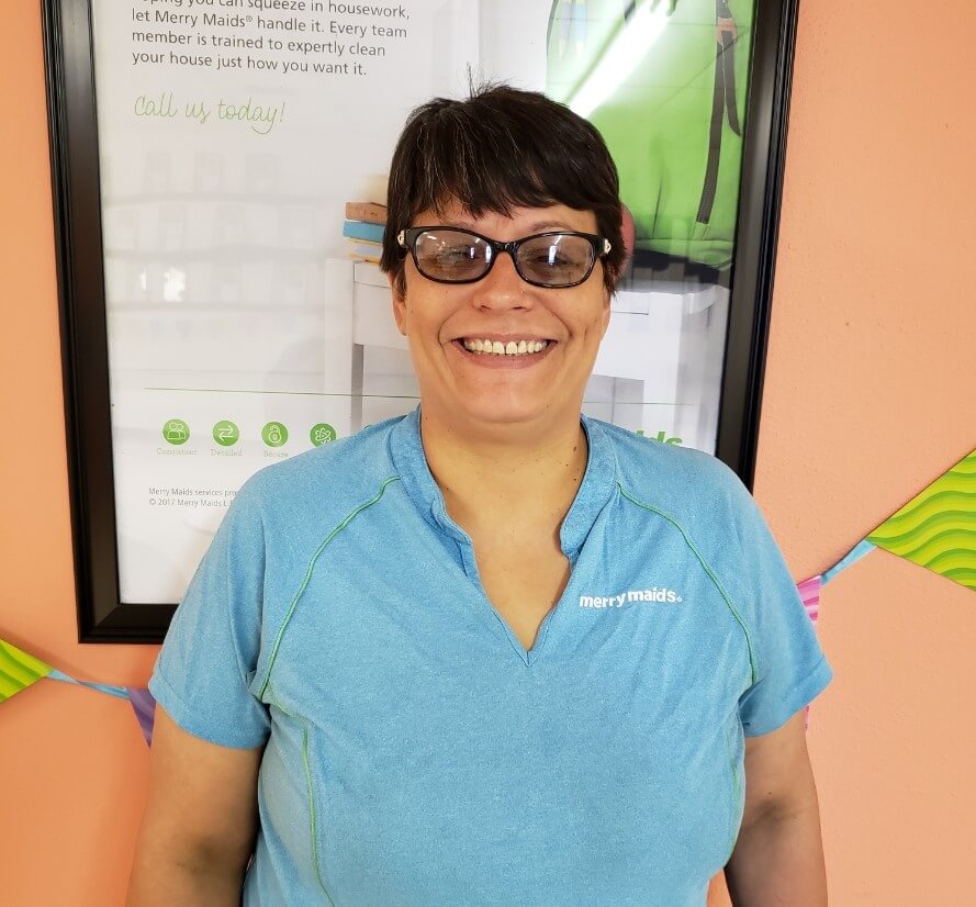 Merry maids team member Sandra Evans in an indoor setting standing in front of a poster.